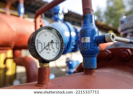 Shallow depth of field (selective focus) details with industrial pressure gauge on an industrial metallic hot water pipeline.