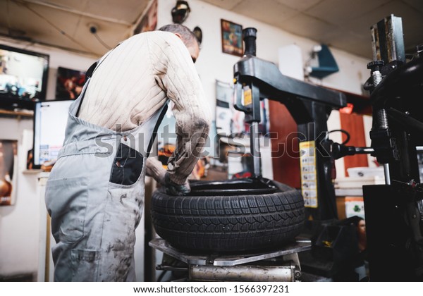 Shallow depth of field (selective focus) image\
with a mechanic changing the regular summer tyres of a car with\
winter tyres in a dirty car\
service.