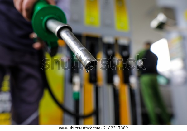 Shallow\
depth of field (selective focus) details with a man holding a fuel\
pump dripping with gasoline in a gas\
station.