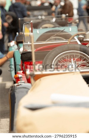 Shallow depth view along the backs of several vintage open-top roadsters parked in a line at a crowded car show. Visible details include spare wire wheels