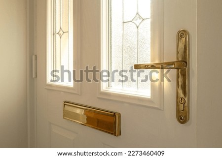 Shallow focus of a brass effect, new generation door lock and handle seen on a newly fitted, double glazed front door. Showing its double glazed, leaded windows.