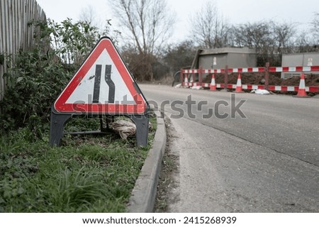 Shallow focus of a British restricted access sign seen on a grass verge at a dangerous road corner. Gas pipes are being laid.