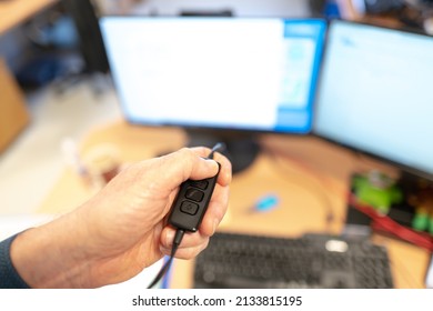 Shallow Focus Of A Call Centre Operative Seen Holding A VoIP Headset Volume Control Switch While Standing Over His Dual Computer Screen Setup.