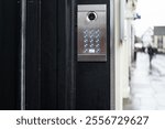 Shallow focus of a generic keypad entry and CCTV system seen at the entrance to a private firm located on a wet high street in the UK.