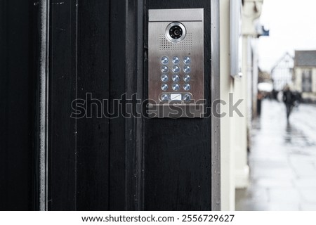 Shallow focus of a generic keypad entry and CCTV system seen at the entrance to a private firm located on a wet high street in the UK.
