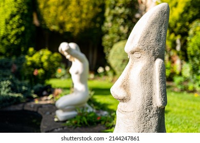 Shallow focus of a home made, stonework face depicting ancient pacific god. Seen on a lawned area in an ornate garden.
