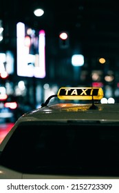 A shallow focus of an illuminated TAXI sign on a car with blurred evening street lights