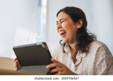 A Shallow Focus Of A Laughing Spanish Woman Using A Tablet Indoors