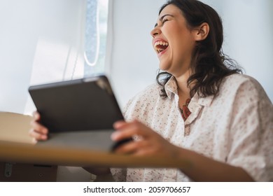 A Shallow Focus Of A Laughing Spanish Woman Using A Tablet Indoors