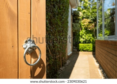 Shallow focus of a newly installed wooden garden gate. Showing the bright metal of the door handle, leading to a lush rear, enclosed garden.