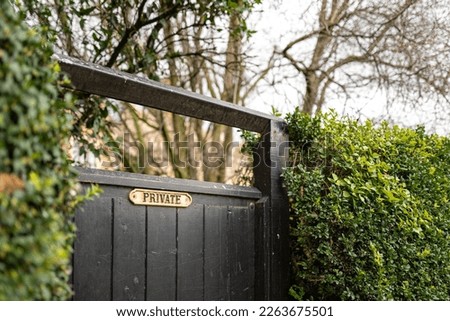 Shallow focus of an ornate, brass Private sign seen on a wooden gate leading to a private garden.