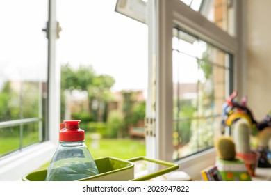 Shallow Focus Of A Part Used Washing Up Bottle Seen In A Sink Area Within A Modern Kitchen. A Kitchen Window Is Open, Looking At To The Large Rear Garden.