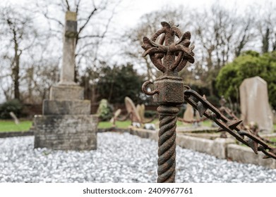 Shallow focus of part of a wrought iron fence post seen near a large tomb and shrine in an old English cemetery.