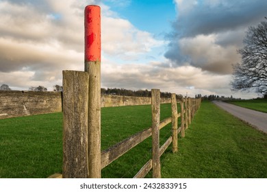 Shallow focus of a red painted post seen along a wooden arable farm fence. An empty road can be seen. Located in mid England near Sherwood Forest.