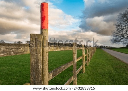 Shallow focus of a red painted post seen along a wooden arable farm fence. An empty road can be seen. Located in mid England near Sherwood Forest.