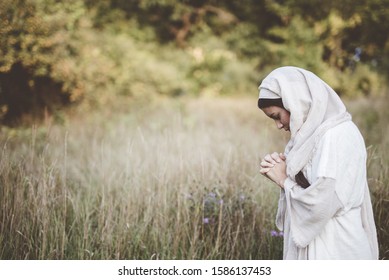 A shallow focus shot of a  female wearing a biblical robe and praying while her eyes are closed