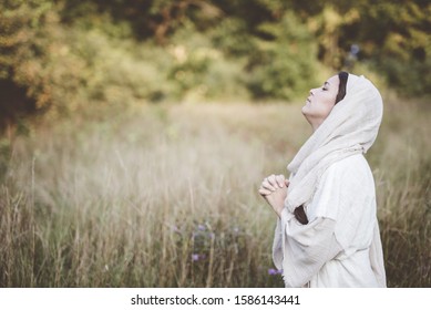 A shallow focus shot of female wearing a biblical robe praying with her head  up towards the sky
