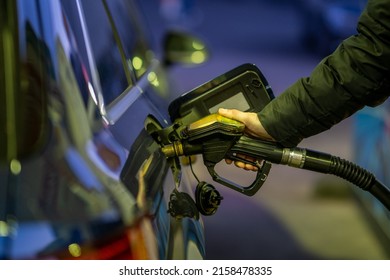 A Shallow Focus Shot Of Hand Of An Adult Man Holding A Gasoline Pump And Filling His Car With Petrol At Gas Station At Night