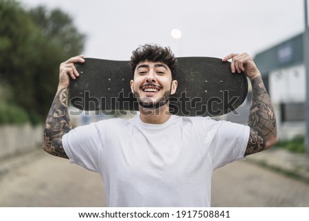 A shallow focus shot of a handsome smiling European skater posing with a skateboard in hands