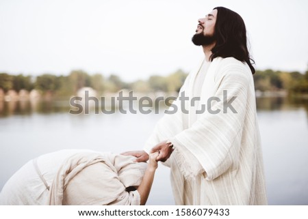 A shallow focus shot of Jesus Christ healing a female with his hand on her head