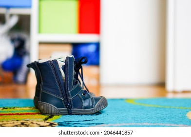 A shallow focus shot of a pair of blue baby boy boots with an open zipper on the colorful carpet