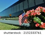 A shallow focus shot of the US flag and flowers in front of the Vietnam Veterans Memorial wall