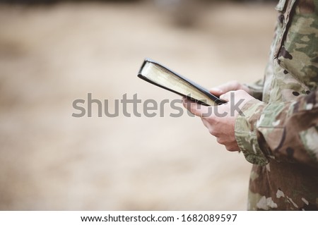 A shallow focus shot of a young soldier holding a bible in a field