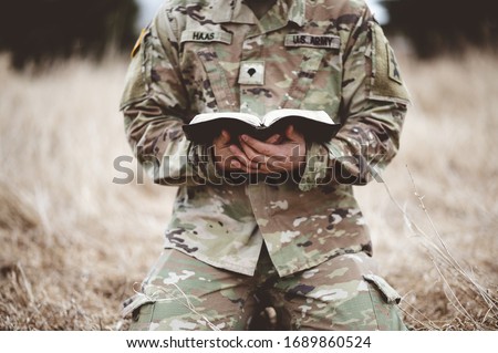 A shallow focus shot of a young soldier kneeling while holding a bible in a field