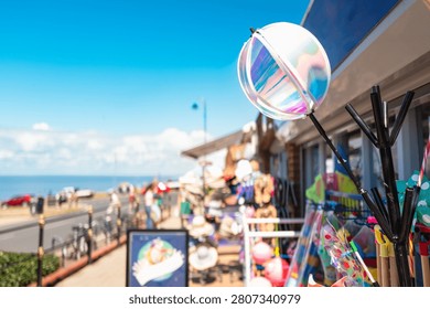 Shallow focus of a spherical wind spinner seen for sale together with other beach items at a typical toy and souvenir shop on the British coast. In the distance is the beach and North Sea.