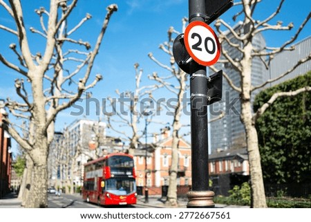 Shallow focus of a typical 20 mph road speed sign attached to a lam post in central London. An iconic London bus can be seen approaching.