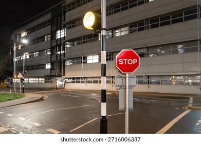 Shallow focus of a typical red Stop sign located by a pedestrian crossing on a medical and science campus in the UK. A science research building is in the background.