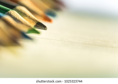 Shallow focus view of a close-up image of new colouring pencils seen on blank writing paper. Detail of some of the colouring pencil tips is evident, seen on a classroom desk.