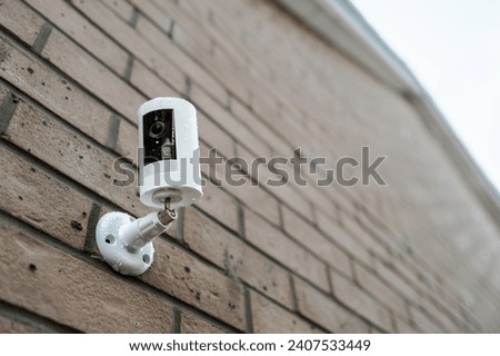 Shallow focus of a wireless smart CCTV night and day camera seen after a heavy downpour on a house exterior wall. The blue motion LED indicator is seen active, showing its recording.
