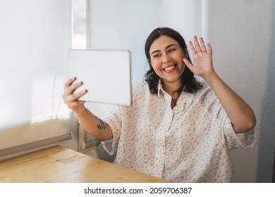 A Shallow Focus Of A Young Spanish Woman Waving At A Tablet Indoors