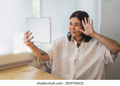 A Shallow Focus Of A Young Spanish Woman Waving At A Tablet Indoors