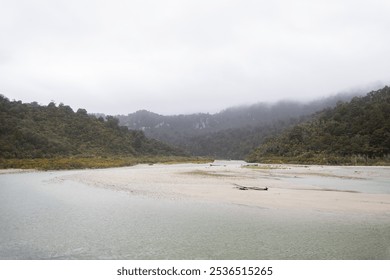 Shallow river flowing through a misty forest valley on a cloudy day - Powered by Shutterstock