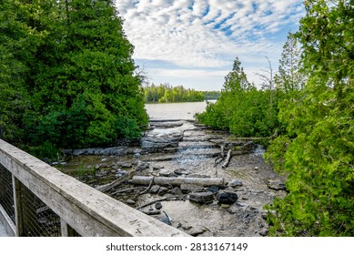 A shallow rocky stream flows through dense forest beside a wooden trail bridge near Cyprus Lake in Bruce Peninsula National Park. Tobermory, Canada - June 23, 2025.