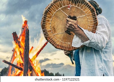 shaman plays drums near the big fire on the sky background