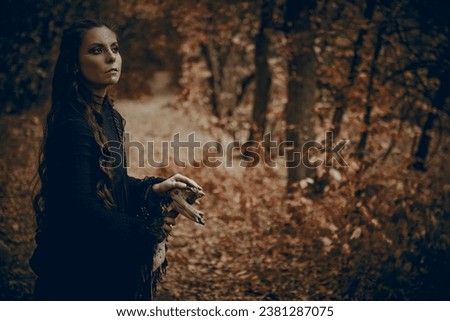 Shamanic rituals. A shaman woman in black garment with ethnic ornaments on her face performs a ritual in an autumn forest. Ethnic culture.