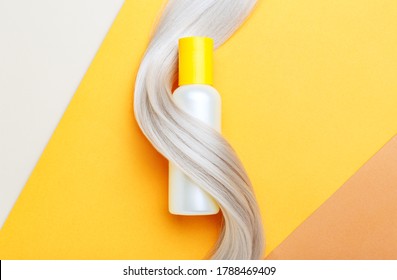 Shampoo Bottle Mockup Strand In Lock Curl Of Blonde Hair On Orange Color Background. Yellow Bottle Shampoo. Flat Lay Copy Space. Hair Care Cosmetics Bath Beauty Products Hair Treatment