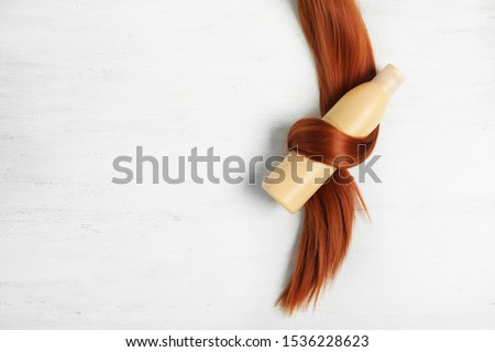 Shampoo bottle wrapped in lock of hair on white wooden background, flat lay with space for text. Natural cosmetic products