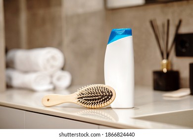 Shampoo and wooden comb on beige table with blurred bathroom background