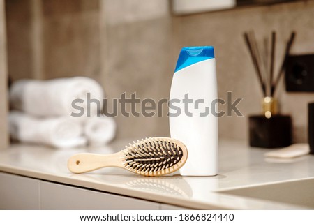 Shampoo and wooden comb on beige table with blurred bathroom background