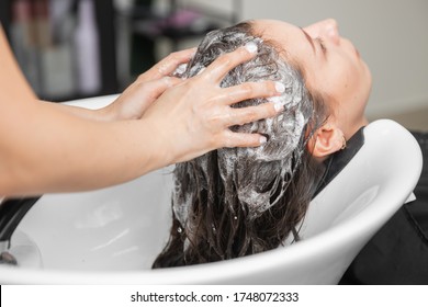 Shampooing hair in spa beauty salon of young brunette woman, hairdresser caring for client.