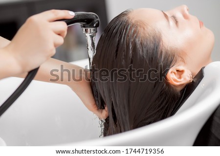 Shampooing hair in spa beauty salon of young brunette woman, hairdresser caring for client.