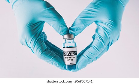 The shape of heart made from hands in gloves holding the covid vaccine booster shot - Shutterstock ID 2069087141