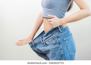 Shape slender, thin waist, attractive slim asian young woman hand show thumb and shape her weight loss, wearing in big, large or oversize jeans, excess lose by diet and exercise, body fit healthy. - Powered by Shutterstock