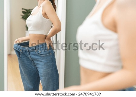 Shape slender, thin waist, slim fit asian young woman, showing body shape her weight loss, happy wearing in big, large or oversize jeans, excess lose by diet and exercise. Healthy lifestyle concept