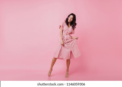 Shapely barefooted lady with tanned skin dancing on pink background. Happy caucasian girl in striped dress fooling around and laughing. - Powered by Shutterstock