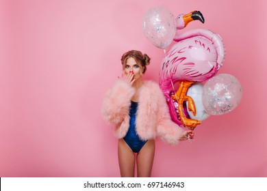 Shapely Curly Girl In Velvet Bodysuit Holding Colorful Balloons For Party And Posing With Surprised Face Expression. Shocked Graceful Young Woman In Pink Jacket Standing Isolated On Bright Background